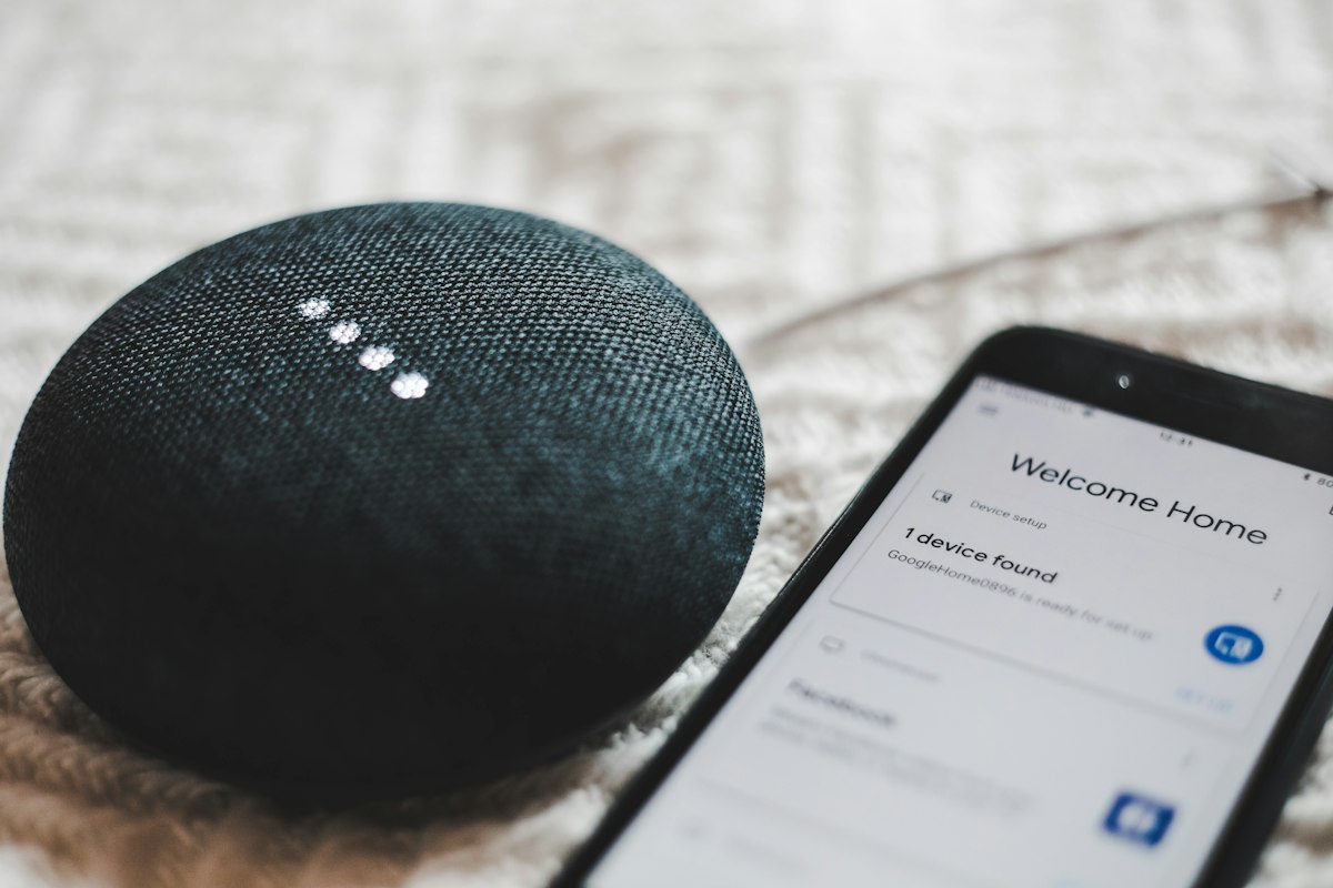 A small smart speaker beside a phone showing a home app