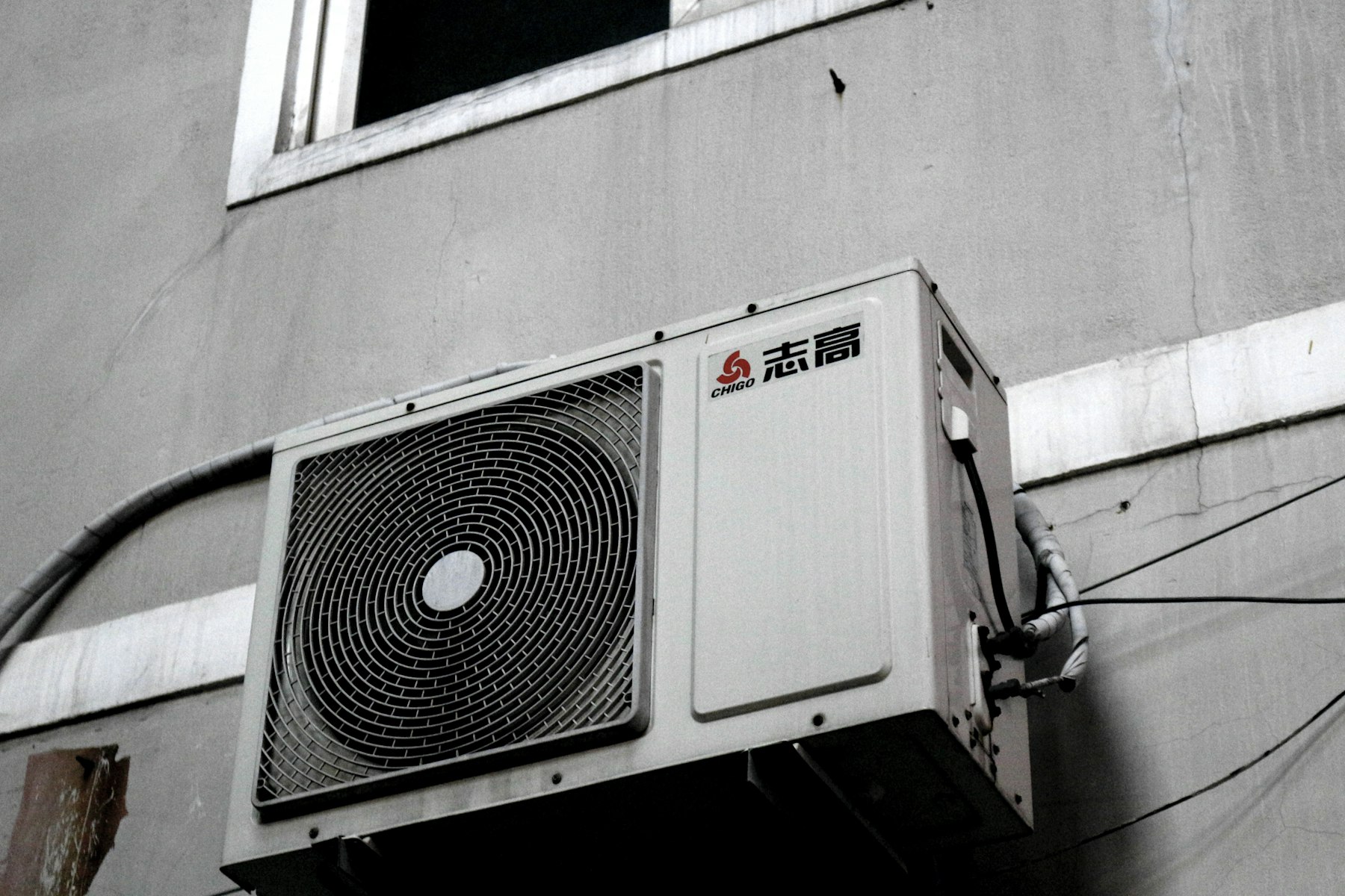 A black and white photograph of an air conditioner condenser on a wall