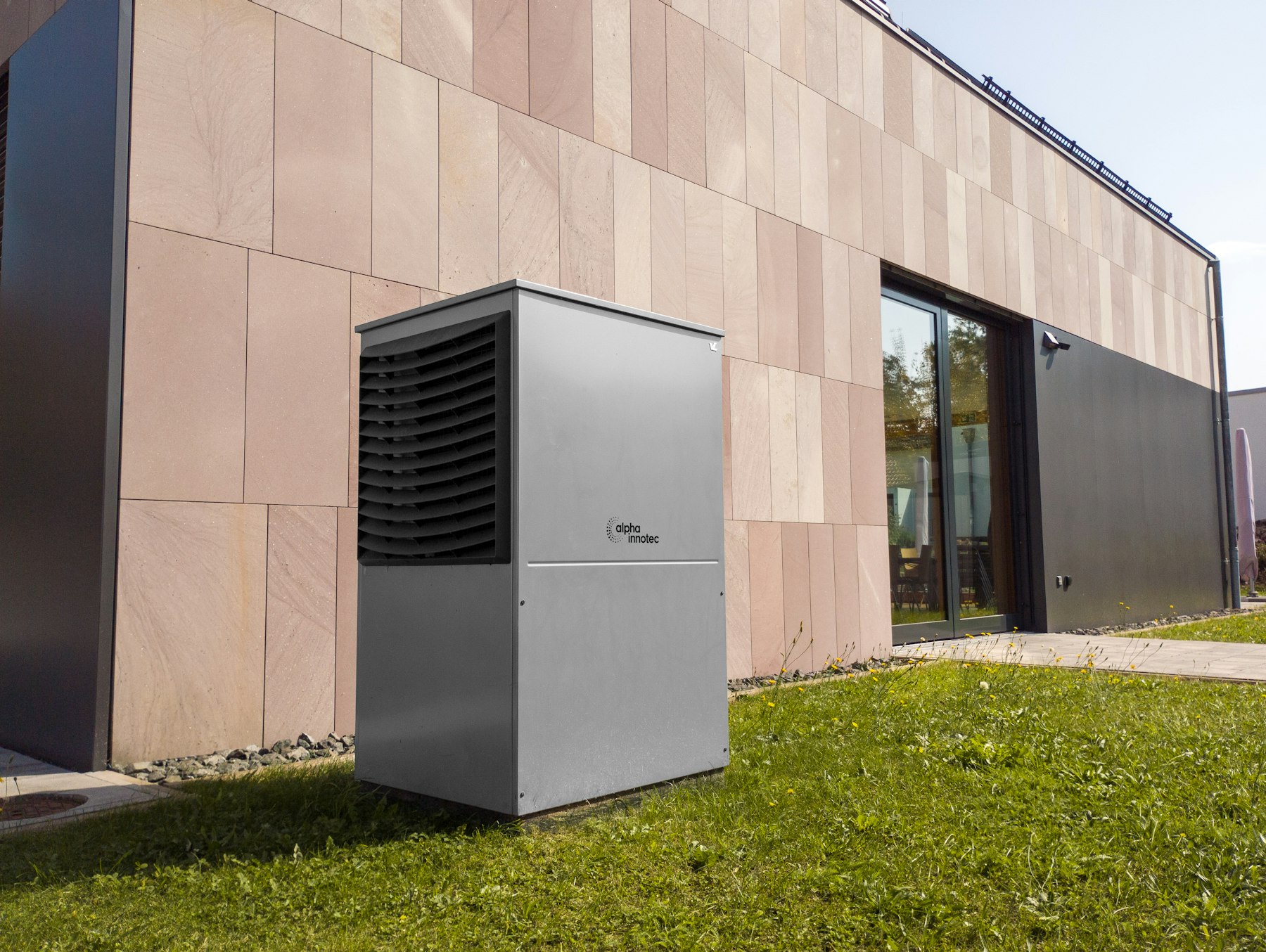 A tall grey heat pump outdoor unit on a lawn beside a modern house