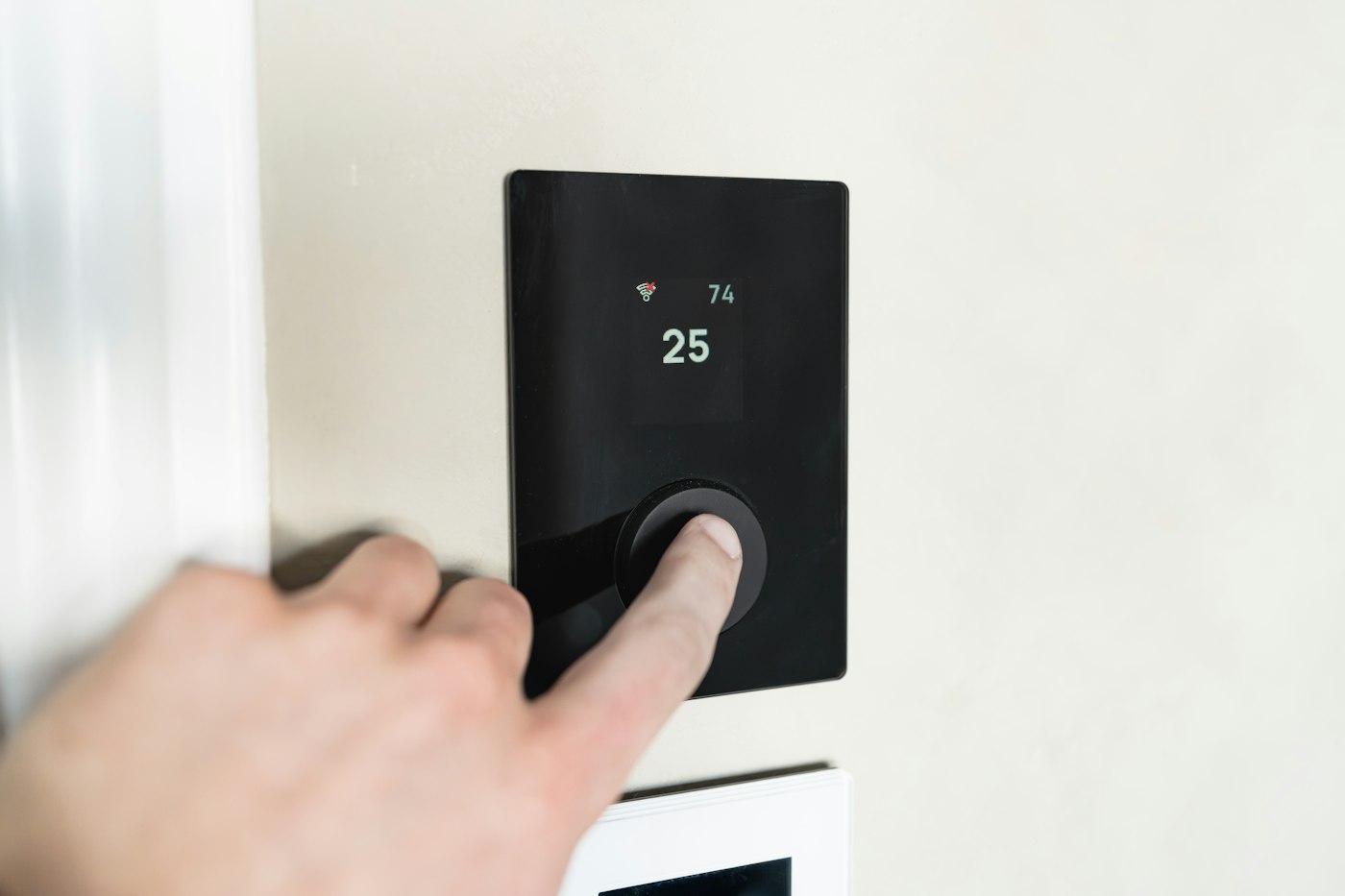 A finger pressing the button on a round wall thermostat